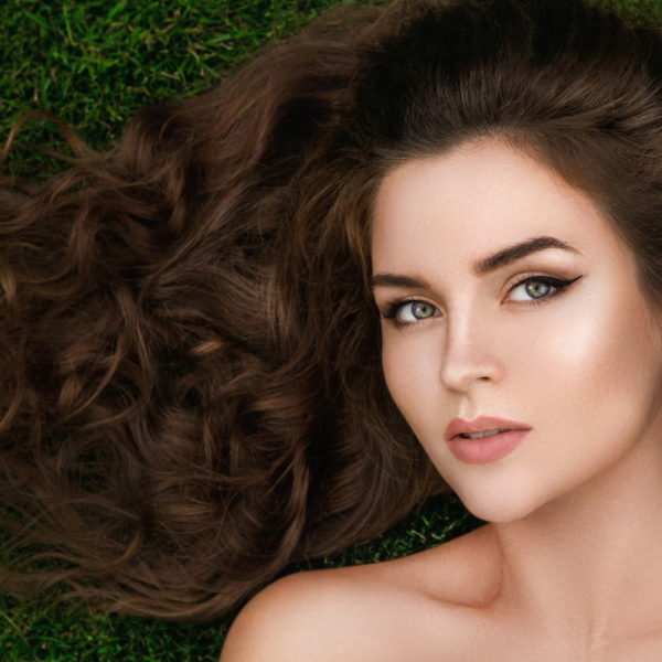 Young and beautiful woman with a healthy curly hair is lying on the grass